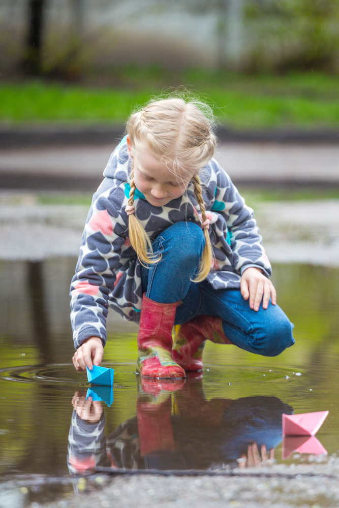 girl runs the pink paper boat in a puddle in the rain, spring