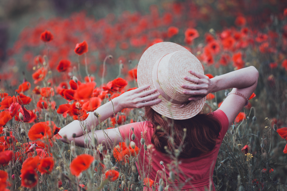 Happy girl in a hat  at the amazing field of beautiful red poppy field  in the countryside.