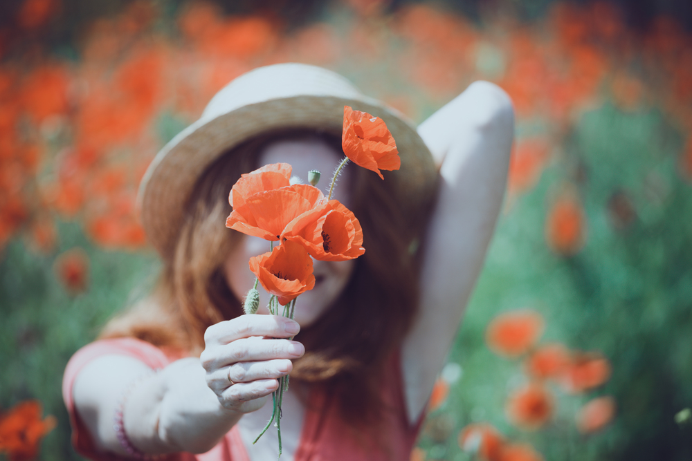Happy girl in a hat  at the amazing field of beautiful red poppy field  in the countryside.