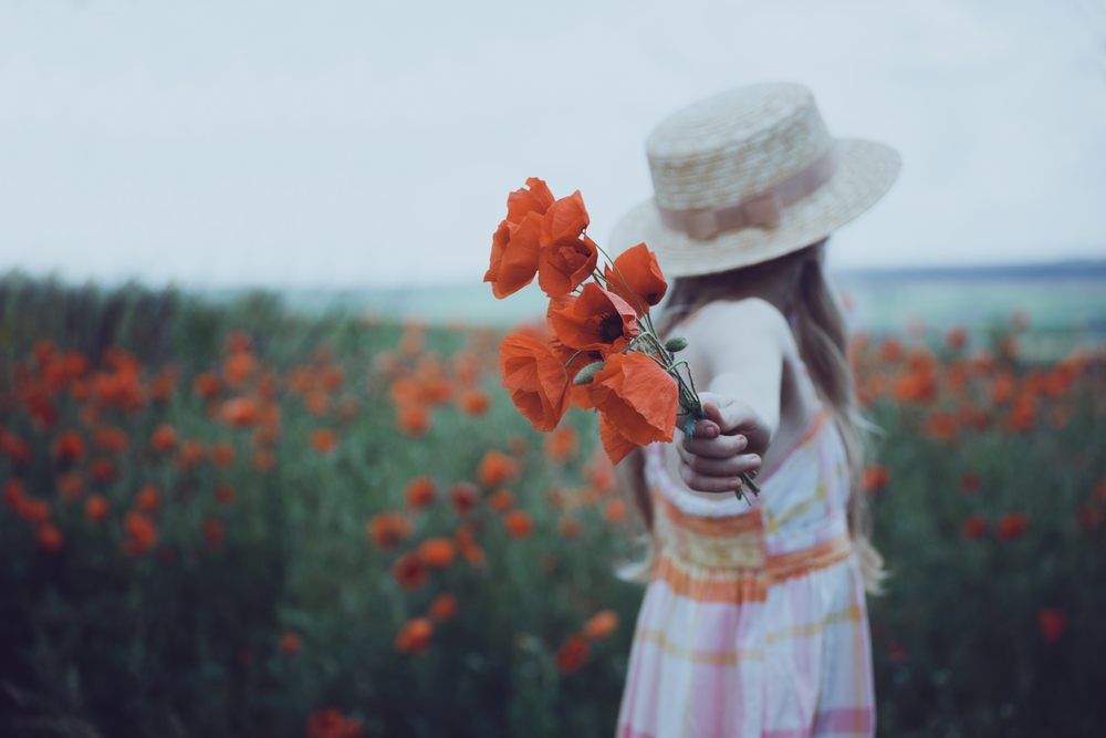 Happy little girl in a hat  at the amazing field of beautiful red poppy field  in the countryside.