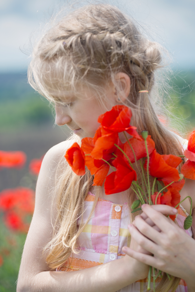 Happy little smiling girl in a hat  at the amazing field of beautiful red poppy field  in the countryside.