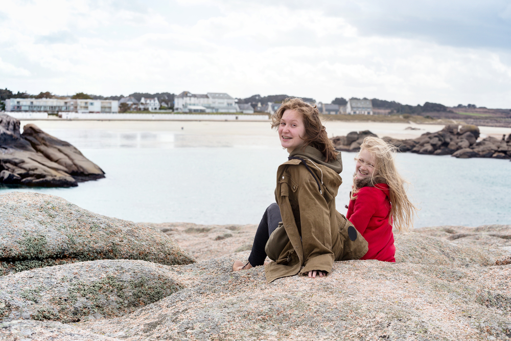 smiling sisters sitting on a bench near the sea and the shore at  the Tregastel, Brittany. France