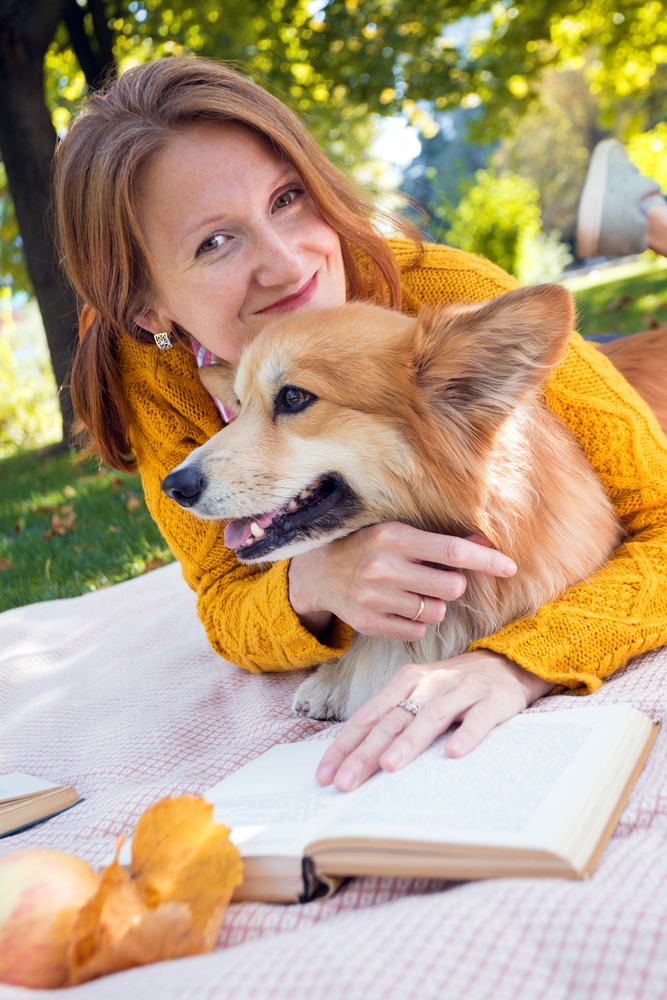 bright fun autumn. girl and dog Corgi  lie on a plaid on the lawn and read books