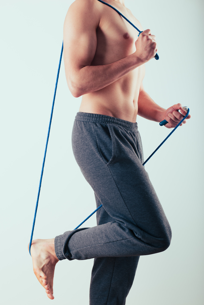 Young man holding skipping rope, doing exercises at home. Portrait orientation