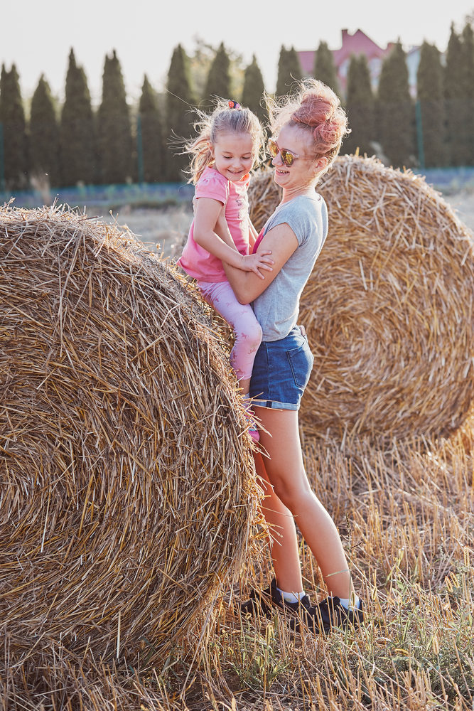 Sisters, teenage girl and her younger sister playing together on hay bale outdoors in the field in the countryside. Candid people, real moments, authentic situations