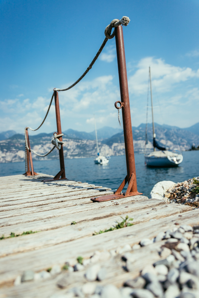 Wooden dock pier in the foreground, sailing boats in the blurry background