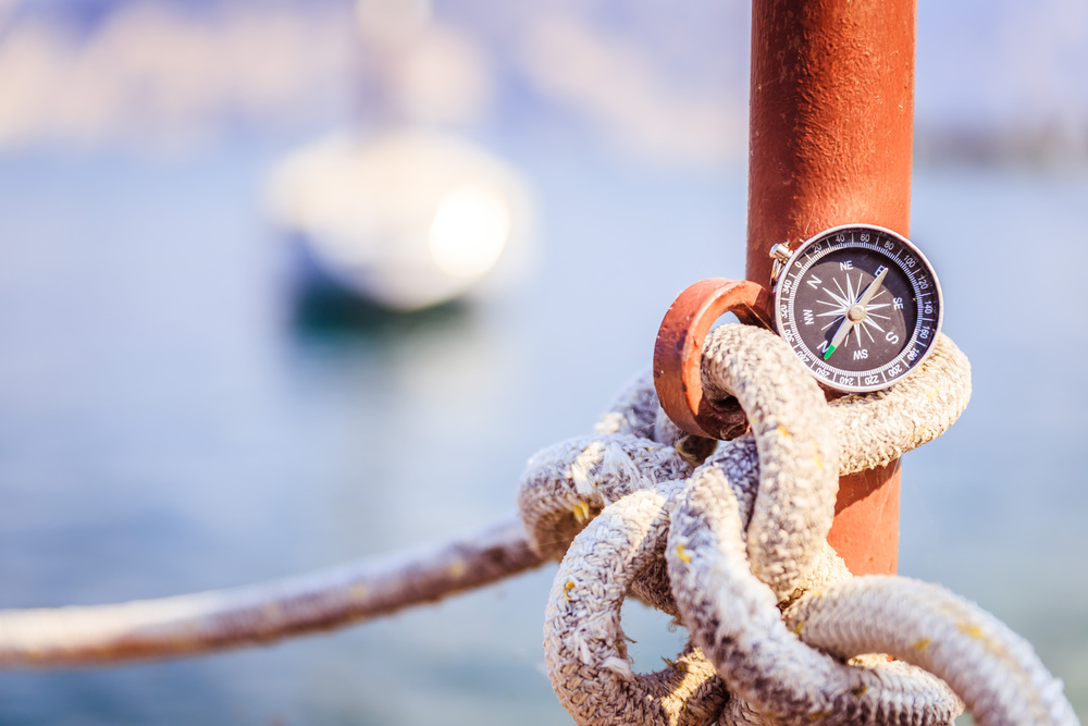 Compass on a lying on a sailing rope, ocean and sailing boats in the blurry background