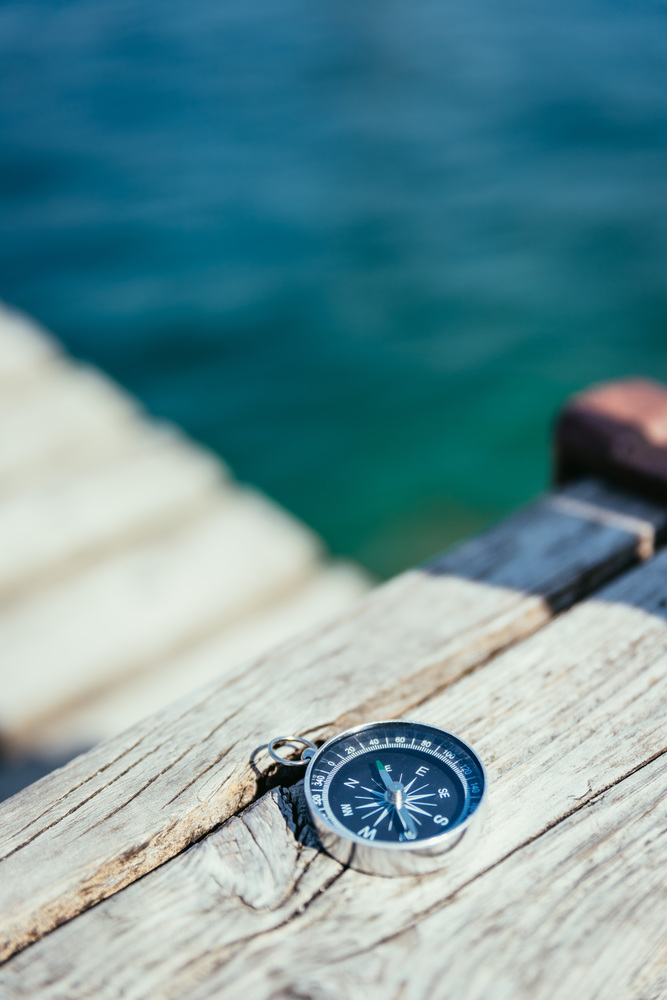 Compass lying on wooden dock pier in the foreground, sailing boats in the blurry background