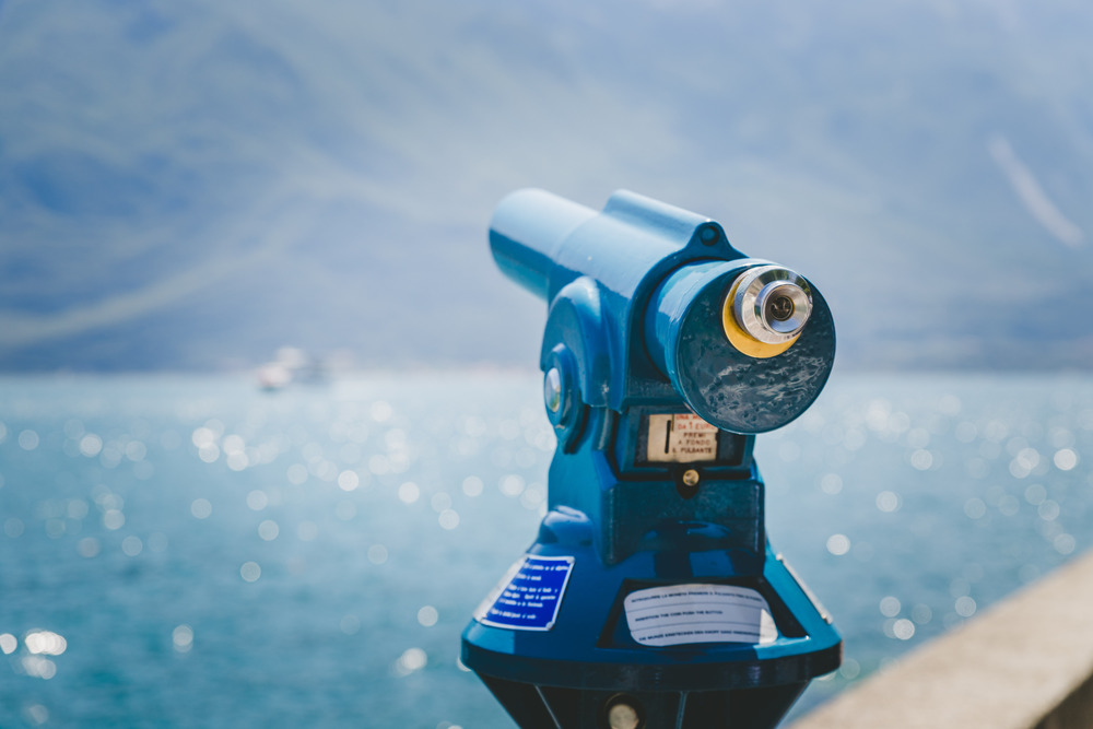 Close up of tourist binoculars at the lake Lago di Garda. Blue water and mountains in the blurry background
