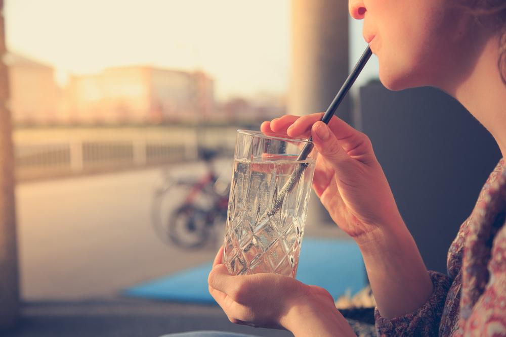 Woman is holding a glass with clear beverage and ice cubes