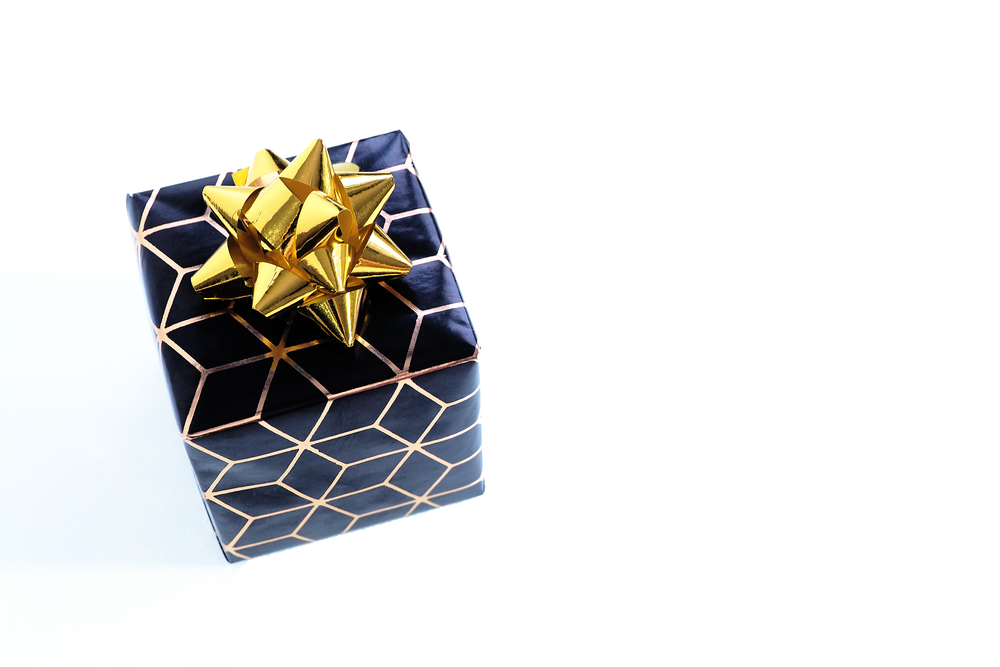 small box in black wrapping paper with a gold geometric pattern and a gold bow. Isolate on a white background.