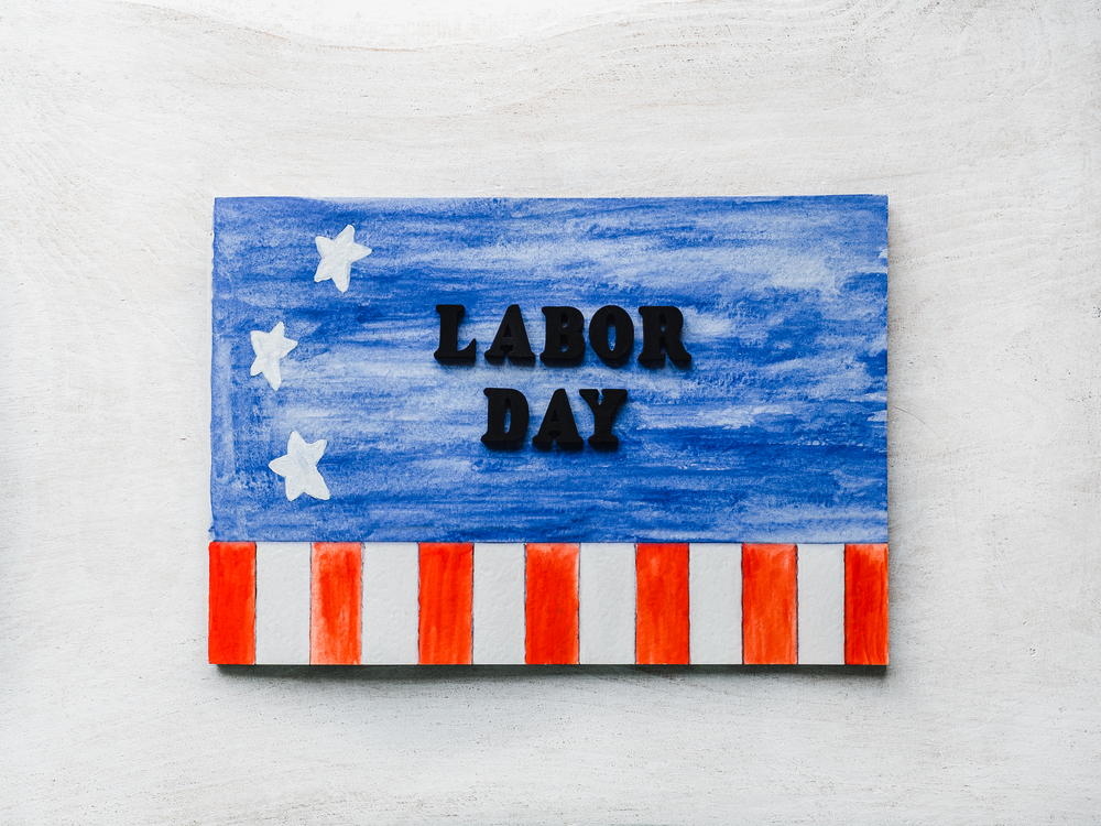 LABOR DAY. Notepad, American flag pattern and wooden letters of the alphabet on a white table. Close-up. Bright photo and space for your inscriptions. Congratulations to relatives, friends, colleagues. Beautiful card with congratulations on Labor Day