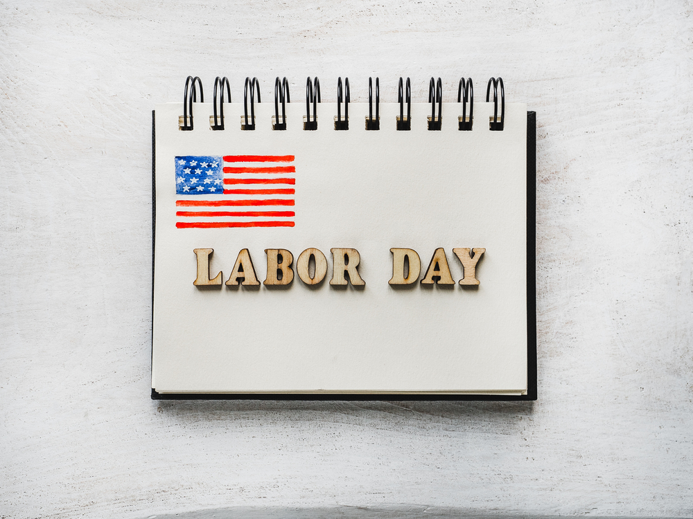 LABOR DAY. Notepad, American flag pattern and wooden letters of the alphabet on a white table. Close-up. Bright photo and space for your inscriptions. Congratulations to relatives, friends, colleagues. Beautiful card with congratulations on Labor Day