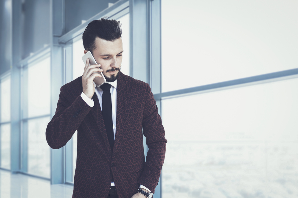 Trendy and fashionable businessman walking inside the corporate building and talking on the phone (mixed)