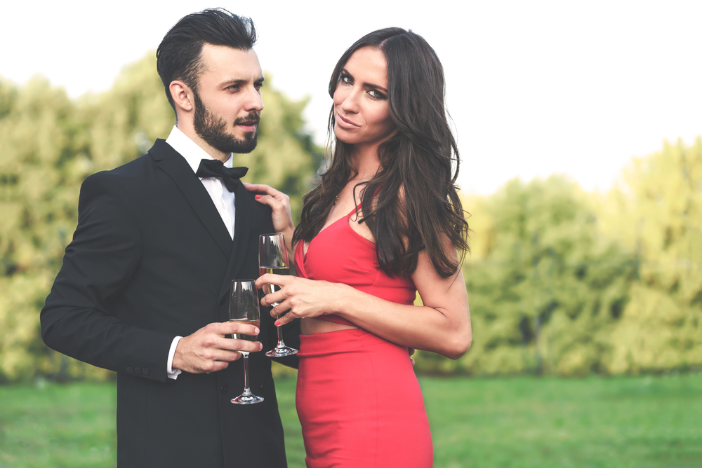 Happy couple of lovers with a glass of wine or champagne standing outdoors in the garden during wedding party or banquet