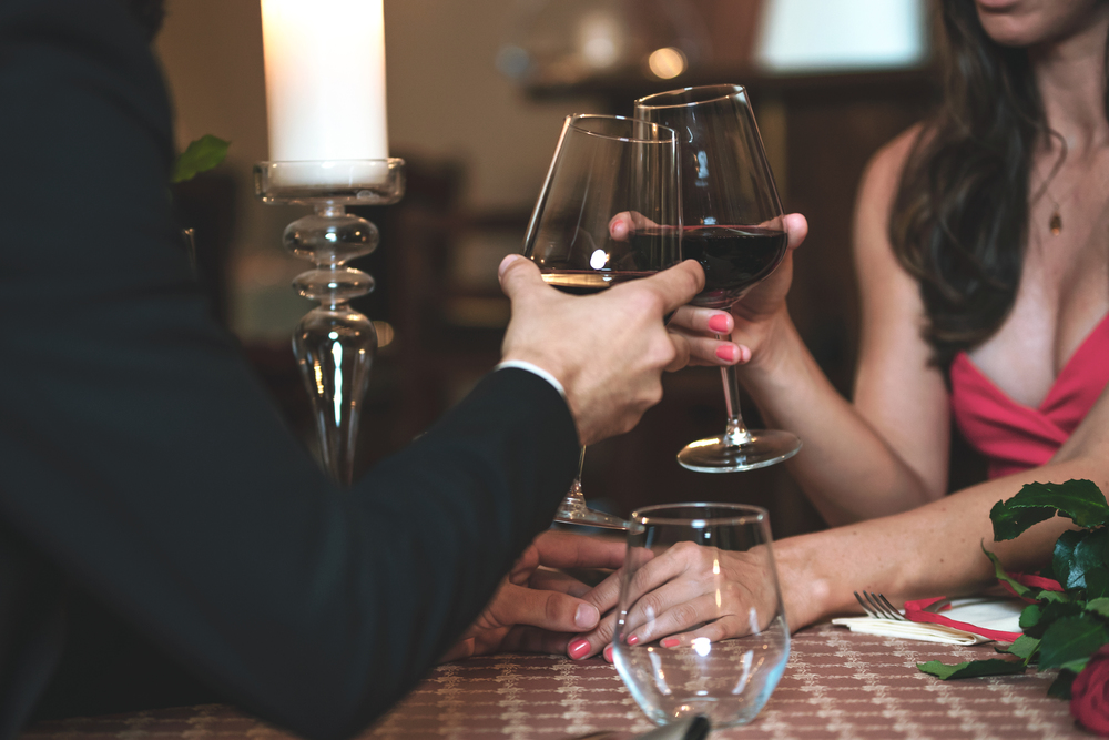 Couple in love holding hands and drinking wine during a romantic dinner in a restaurant (reduced tone)