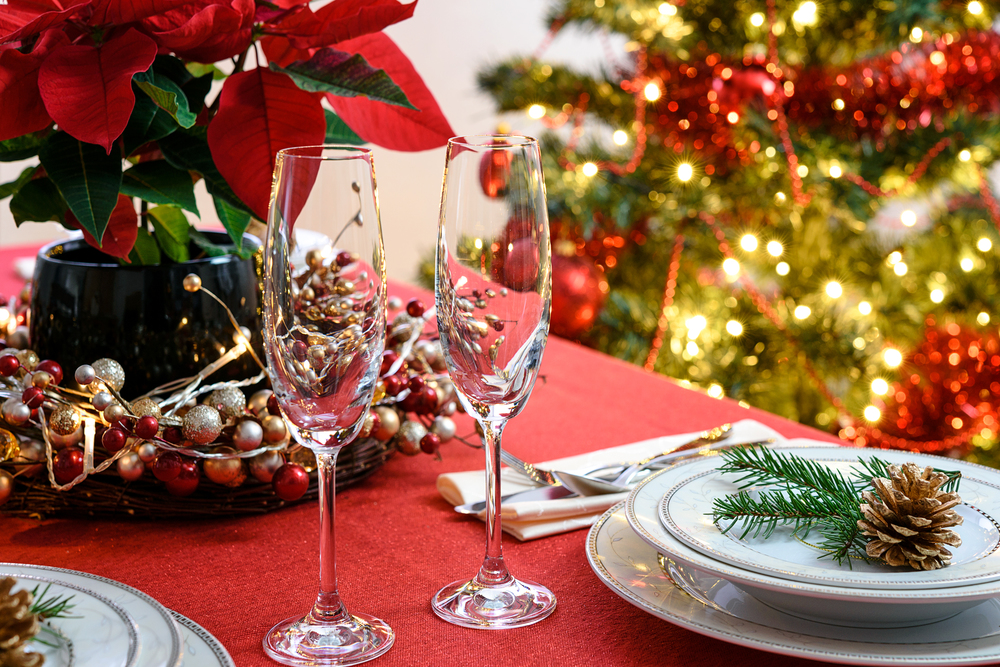 Christmas or New Years table decoration concept - champagne glasses, red poinsettia and table setting on a background of colorful Christmas decoration.