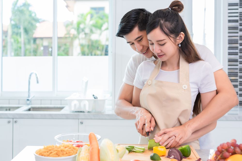 Asian couples cooking and slicing vegetable in kitchen together. Man teaching woman to preparing meal in home. People and lifestyles. Holiday and Honeymoon concept. Valentine day and wedding theme