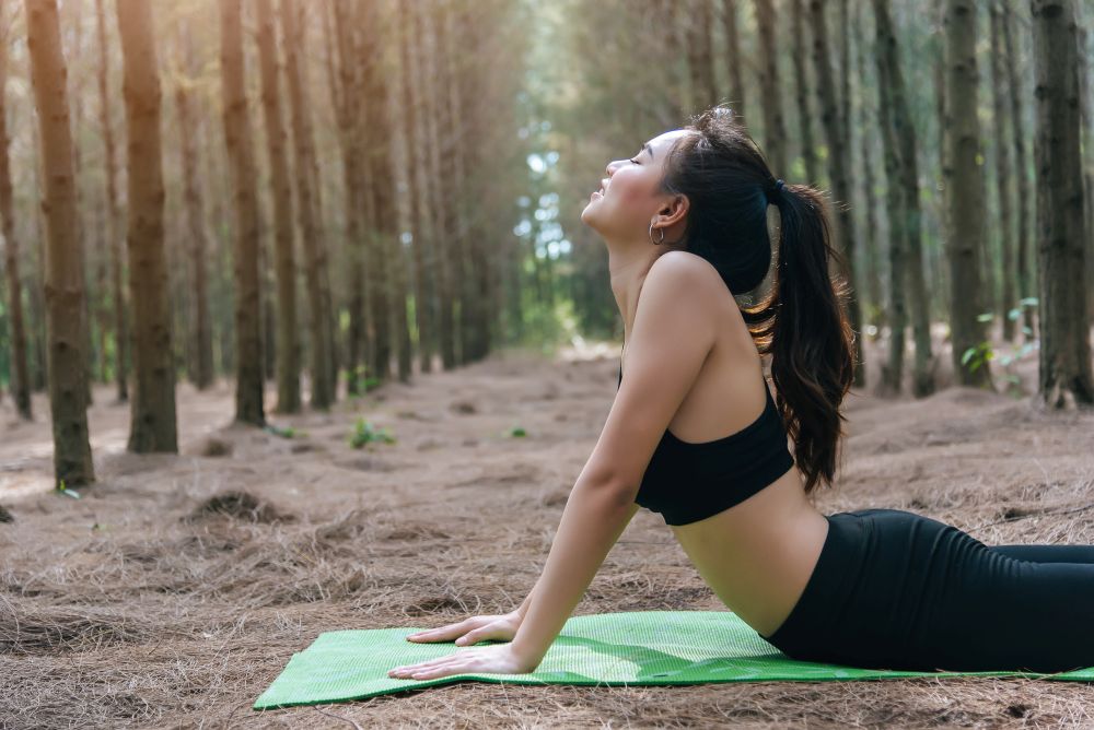 Beautiful Asian young woman doing yoga and planking on green mat in forest. Exercise and meditation concept. Peaceful and countryside concept
