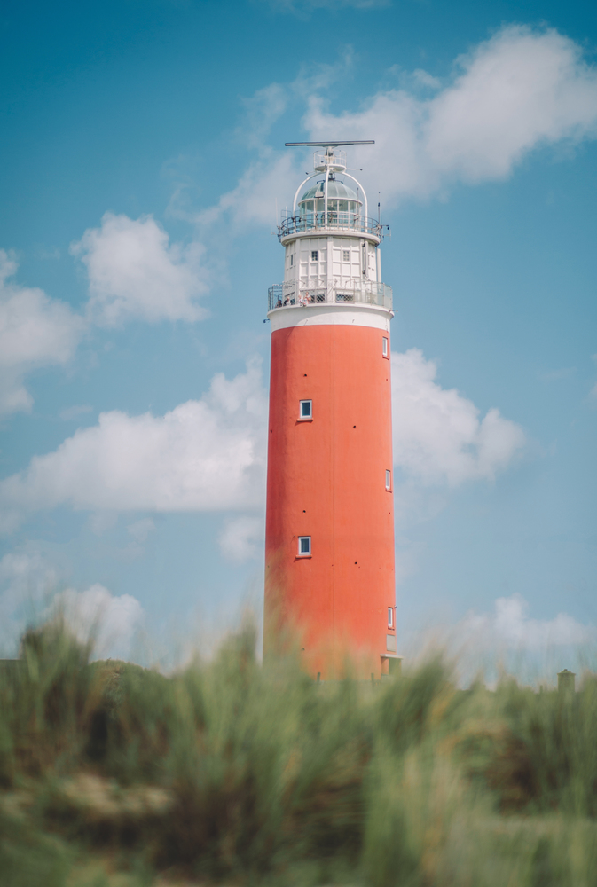 The lighthouse of the island of Texel in The Netherlands surrounded by tall sand dunes in beautiful sunlight and cloudy sky