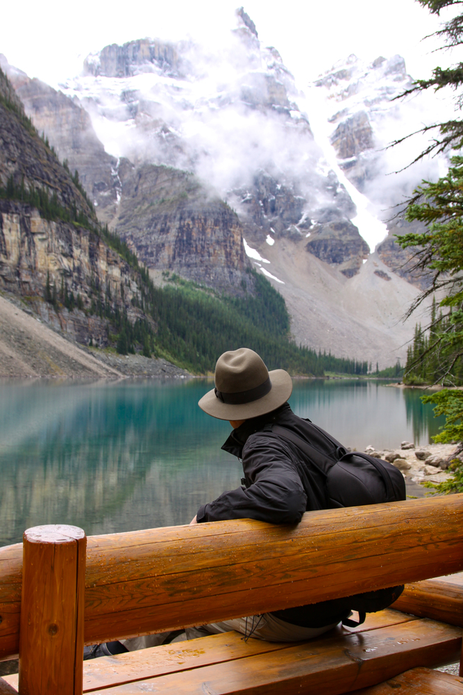 Hiker pauses on wooden bench at Lake Moraine Lake