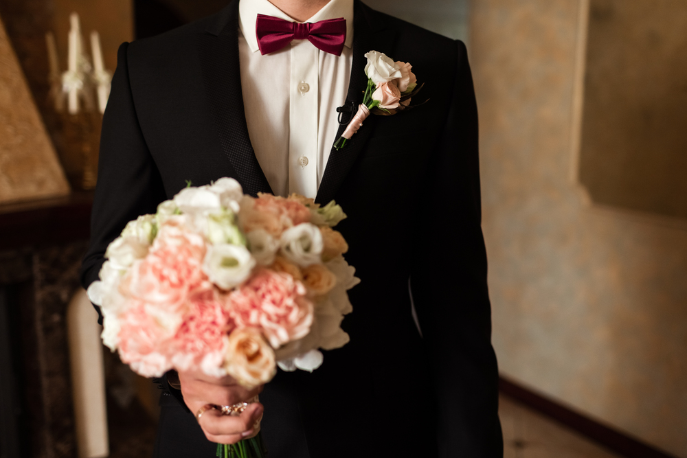 Close-up of a cropped frame is a tender bouquet of roses in the hands of a groom. A men in a wedding suit with tie is holding flowers. Close-up of a cropped frame is a tender bouquet of roses in the hands of a groom.