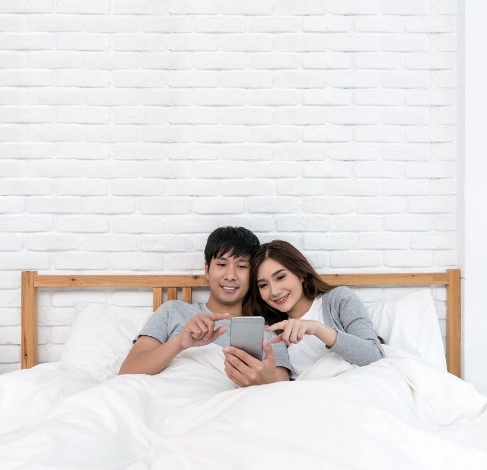 Happy Asian Lover using the technology smart phone for selfie on the bed in bedroom at home, Couple selfie concept,