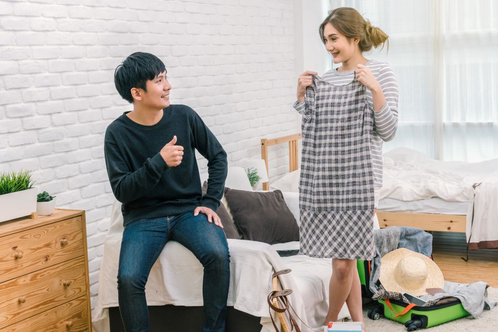 Happy Asian Couple choosing the clothes for preparing to travel in living room at the modern home, Couple, life style and traveler concept,