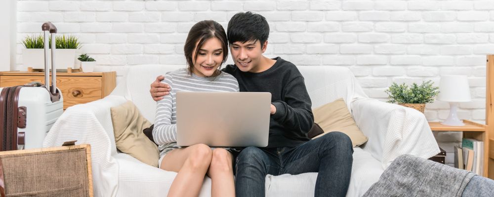 Banner and cover scene of Happy Asian Couple planning and booking the hotel for travel with technology laptop on the sofa of living room at the modern home, Couple, life style and traveler concept,