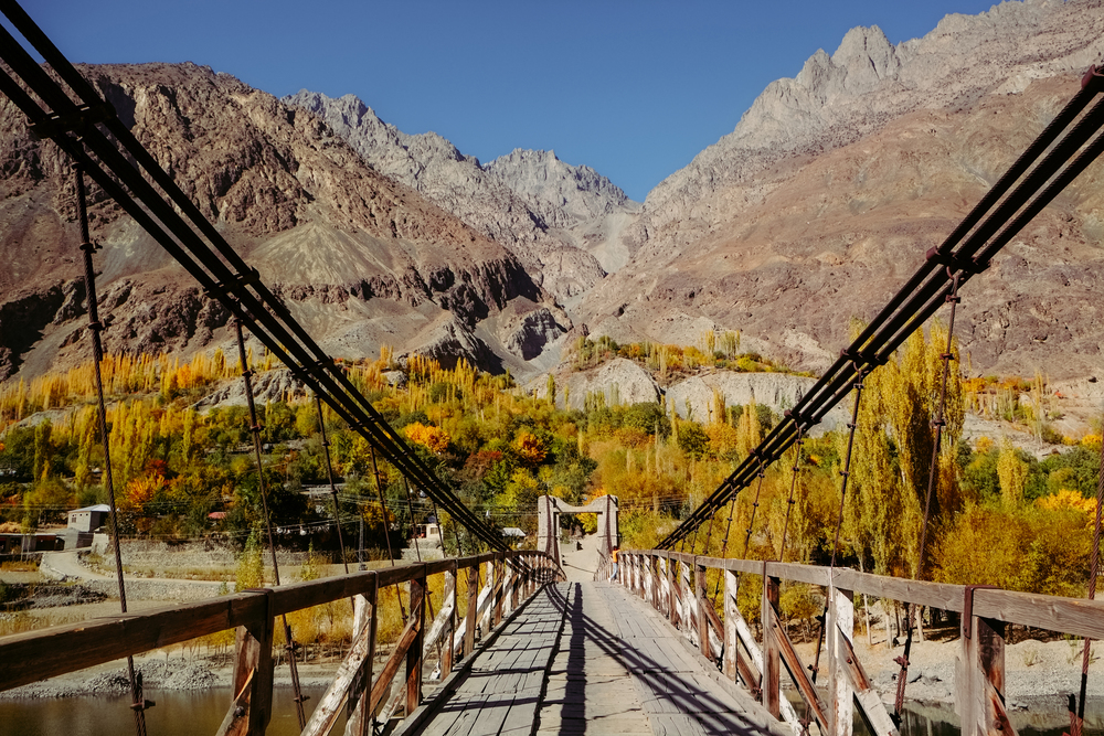 Wooden suspension bridge leads to Khalti village. Colorful nature landscape view in autumn season against Hindu Kush mountain range, Gupis Ghizer valley. Gilgit Baltistan, Pakistan.