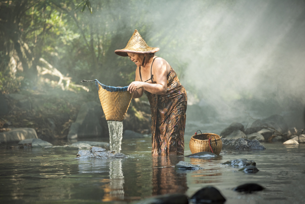 Old woman asian citizen grandmother elderly serious shower and fishing with bamboo basket on river stream nature in countryside of living life senior woman farmer rural people