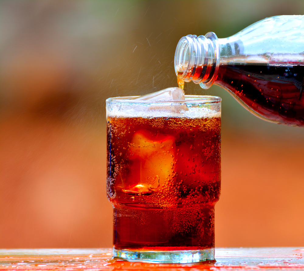 Cola drink is poured into a glass with ice.