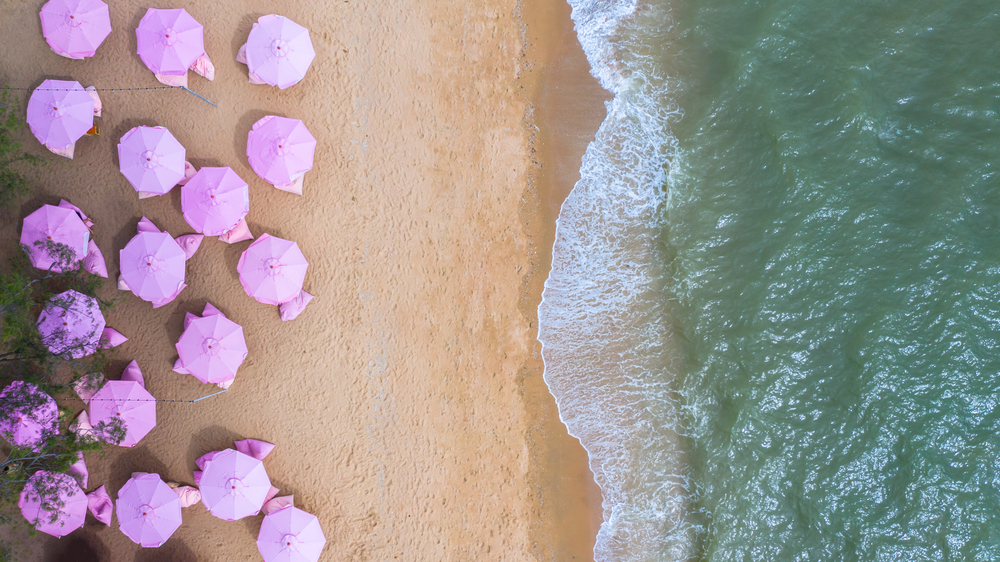 Aerial top view on the sandy beach. Pink umbrellas, sand, beach chairs and sea waves.