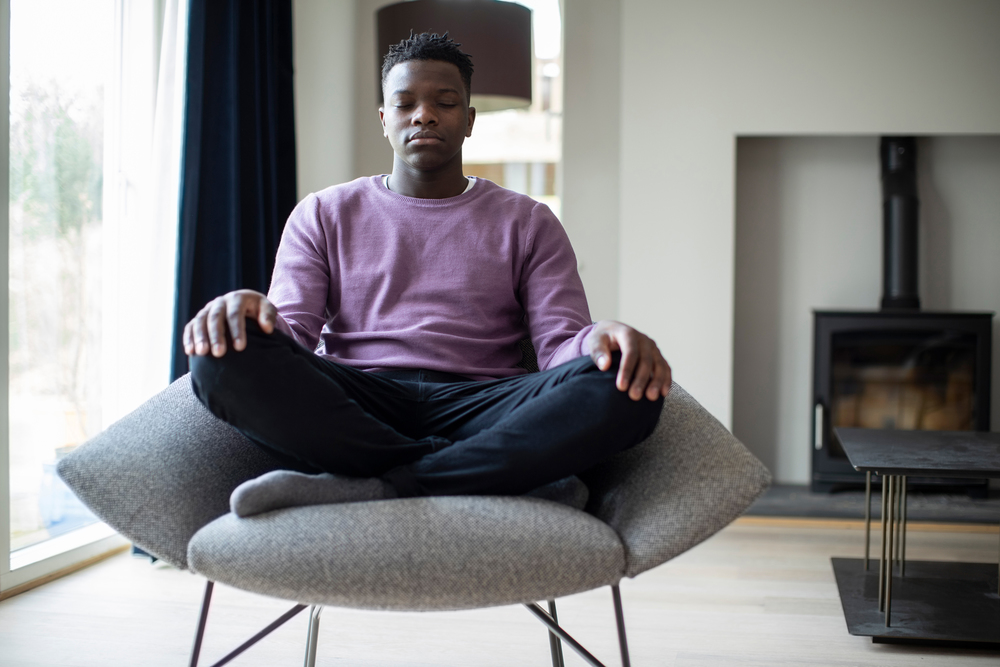 Peaceful Teenage Boy Meditating Sitting In Chair At Home