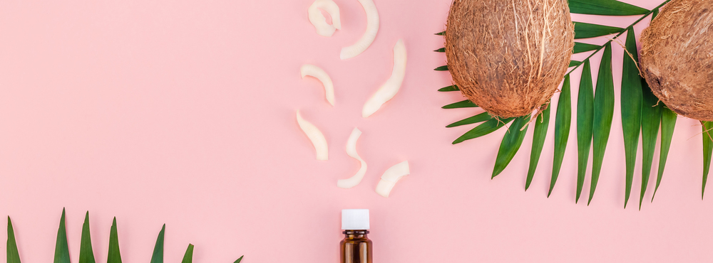 Creative flat lay top view of green tropical palm leaves coconut fruits and coconut oil cosmetics for skin and hair care on pink paper background copy space. Minimal tropical summer beauty spa concept