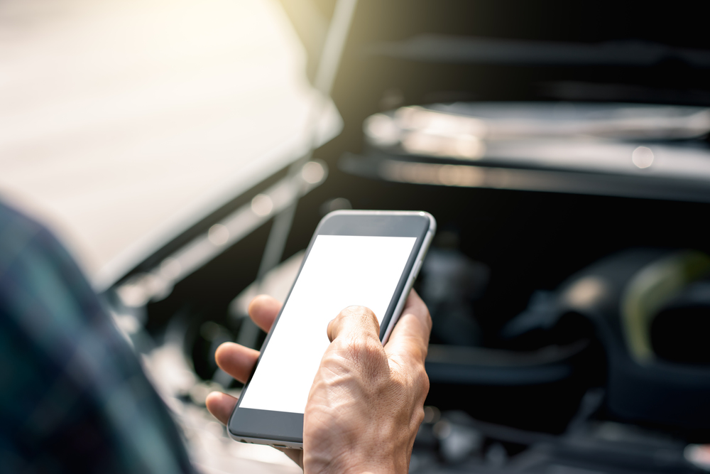 A man&rsquo;s hand is using a smartphone on a traffic road while a car crashes.