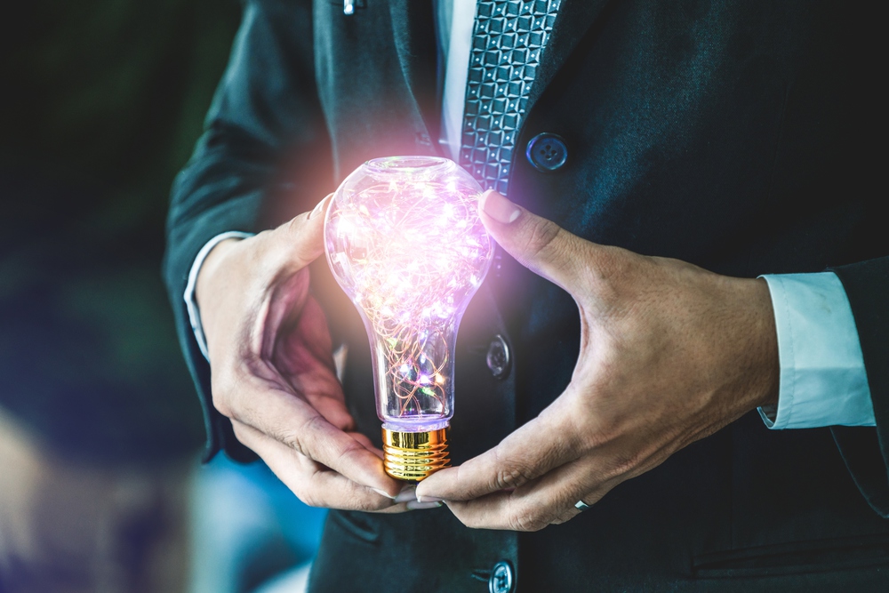 Businessman holding glowing light bulb in hands. Concept of business creativity and ideas.