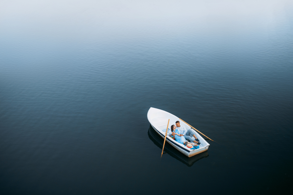Love couple lying in a boat on silent lake, top view. Romantic meeting, boating trip, man and woman walking along the river. Love couple lying in a boat on lake, top view
