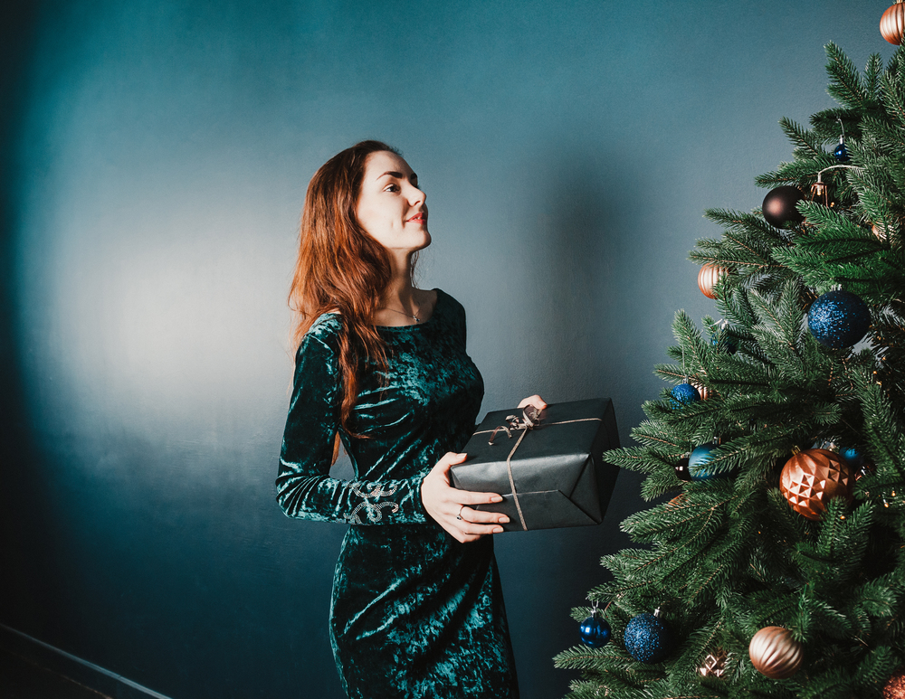 Beautiful girl with a gift box near Christmas tree, smiling. New Year and Christmas concept. Home and family warmth. Copy space for your text and design