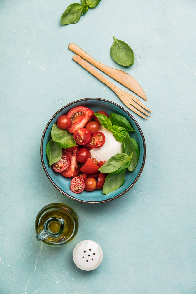 Caprese salad. Mozzarella cheese, tomatoes and basil herb leaves. Blue background. Top view. Caprese salad on blue background