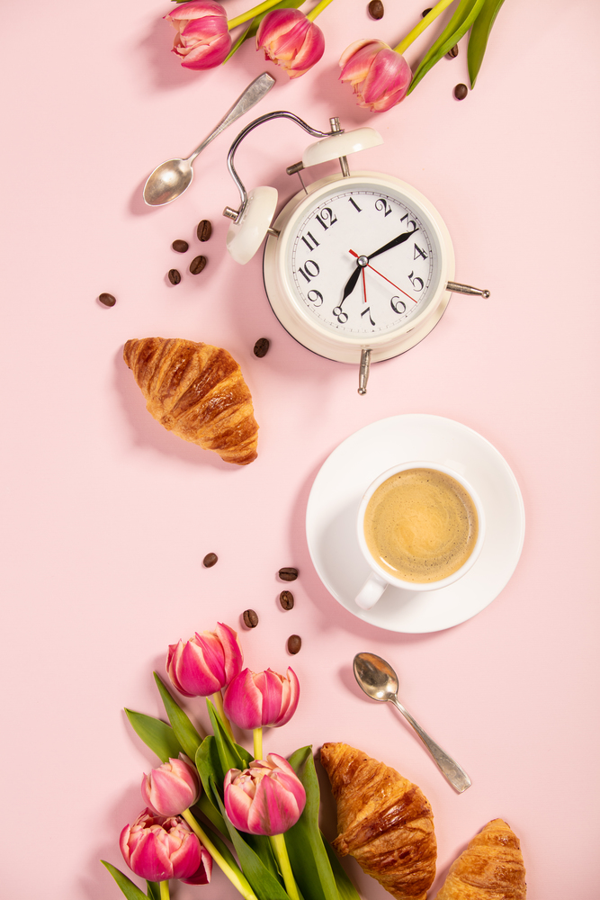 Morning coffee, croissants, alarm clock and a beautiful flowers. Cozy breakfast. Flat lay composition for bloggers, magazines, web designers, social media and artists.
