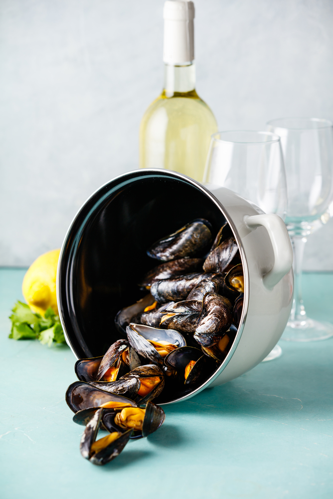 Pot of steamed mussels with lemon, herbs and white wine on blue background. Shellfish seafood.