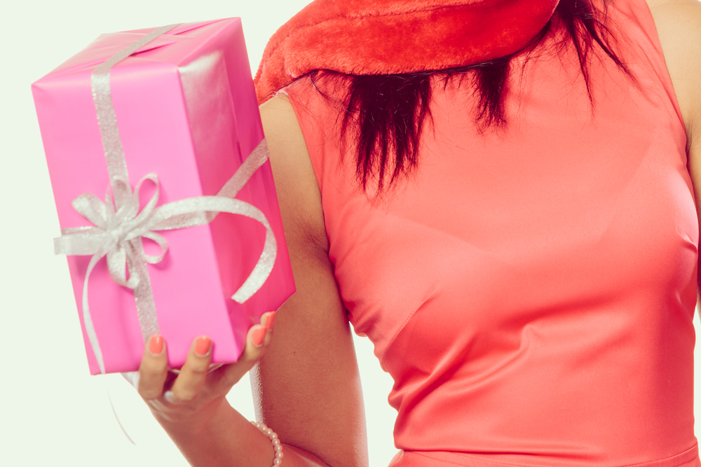 Christmas winter happiness concept. Girl mixed race woman wearing red dress santa helper hat holding pink present gift box filtered photo