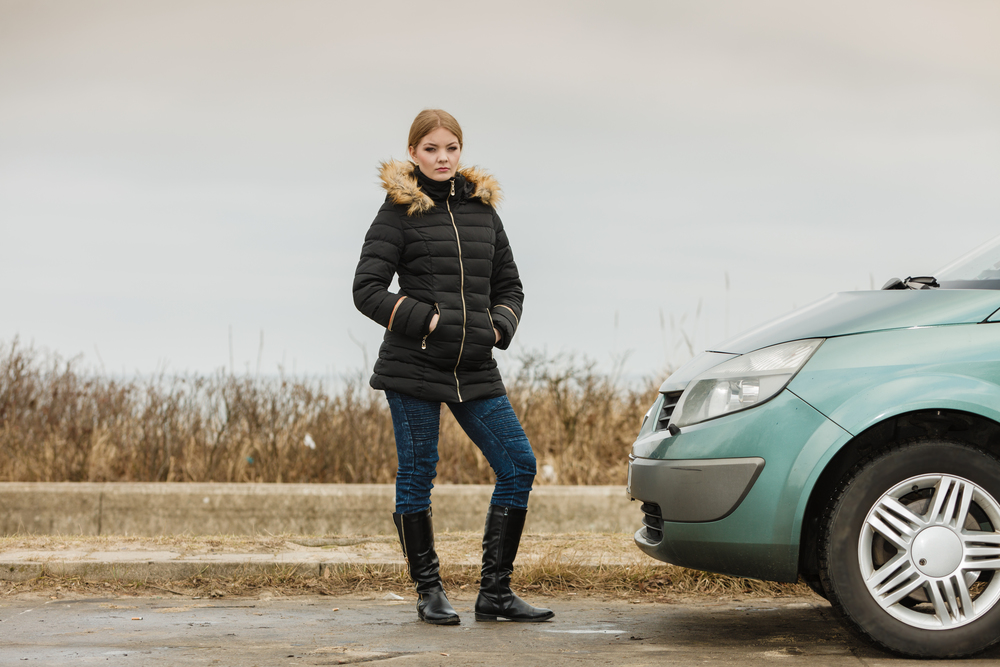 Auto traveling concept. Blonde driver woman in winter clothes standing next to her car.. Blonde driver woman standing next to car