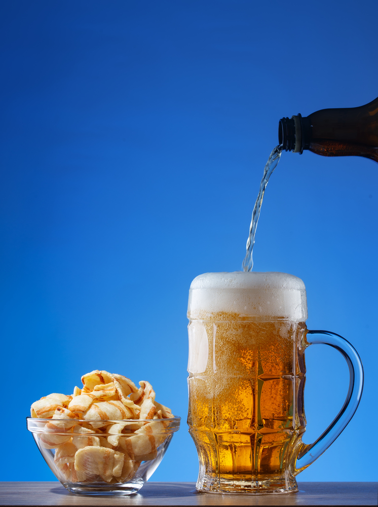 Light beer poured into a mug and snacks in a transparent plate on a blue background. Light beer poured into mug and snacks in plate on blue background