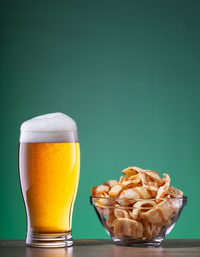 Light beer with foam in a glass and snacks in a transparent plate on a green background. Light beer with foam in glass and snacks in transparent plate on green background