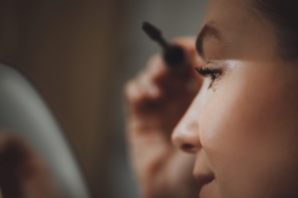 Closeup photo of a gorgeous female doing her makeup at home. Applying mascara to eyelashes. Preparing to festive evening. Beautiful young lady.. Woman doing her makeup at home