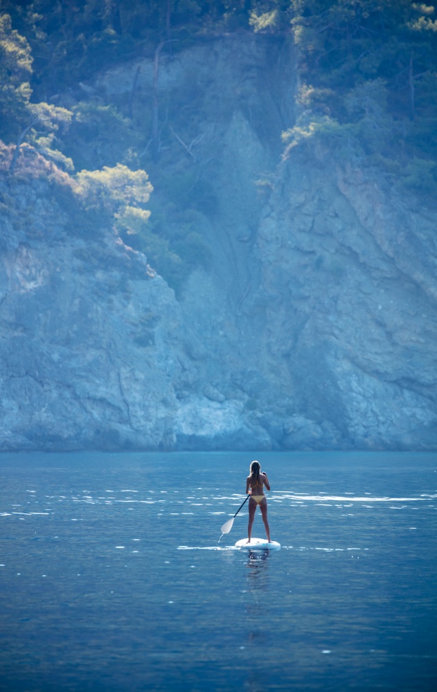 Beautiful sea view under majestic high mountains. Sportive young woman floating on glanders among this beautiful backwater. Riding on the sup.. Sportive woman on the sup
