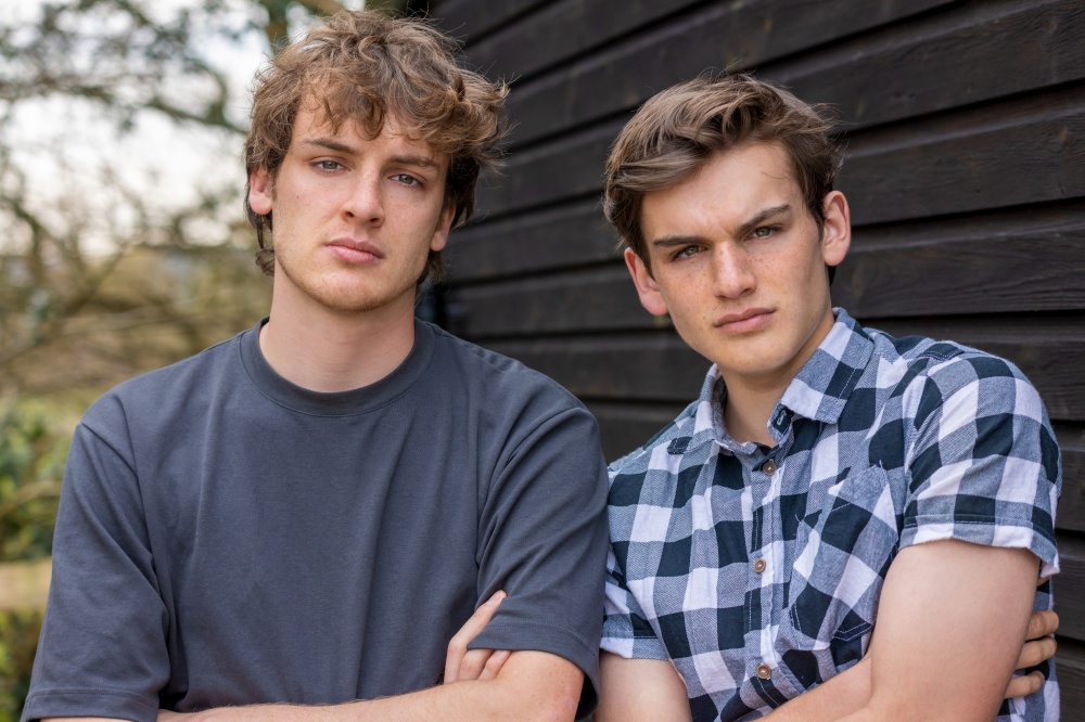 Two handsome thoughtful teenager teen male boy teens young men adults brothers outside arms folded looking to camera
