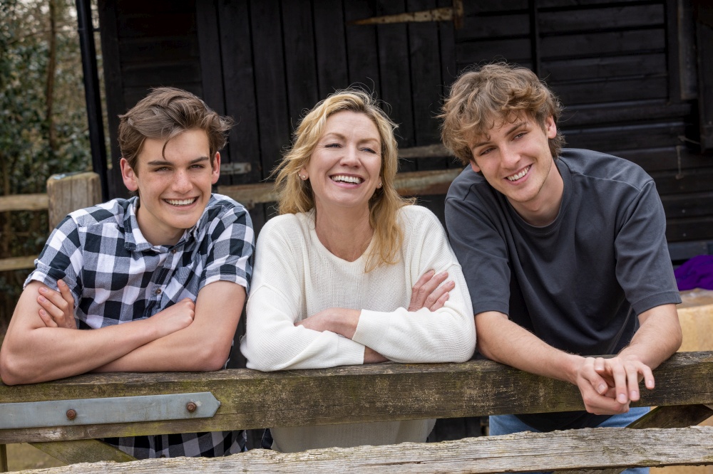 Family of mother and two teenage young men adult sons boys outside leaning on a fence laughing smiling happy together